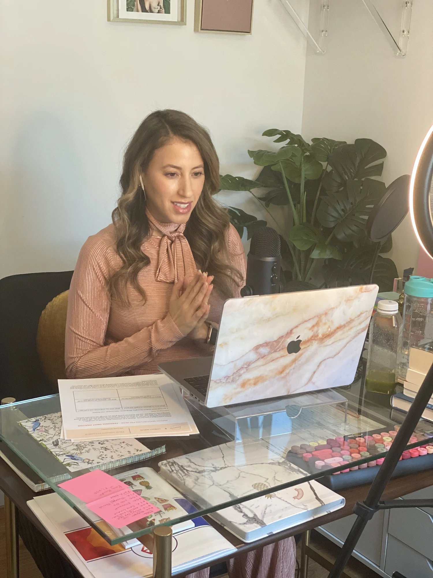 Vanessa Santos at her desk recording with a microphone and ring light, planners and notebooks in front of her